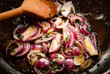 Close up of red onions frying in oil, in a pan with a wooden spoon