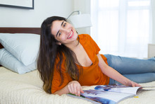 Hispanic Woman Reading Magazine On Bed
