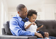 © Mike Kemp/Blend Images - Father and son playing with cell phone on sofa