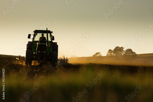 Cuadros en Lienzo Tractor en la puesta del sol arando el campo
