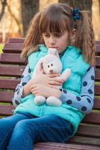 The Sad Little Girl With  Toy Hare Sitting On Bench In  Park