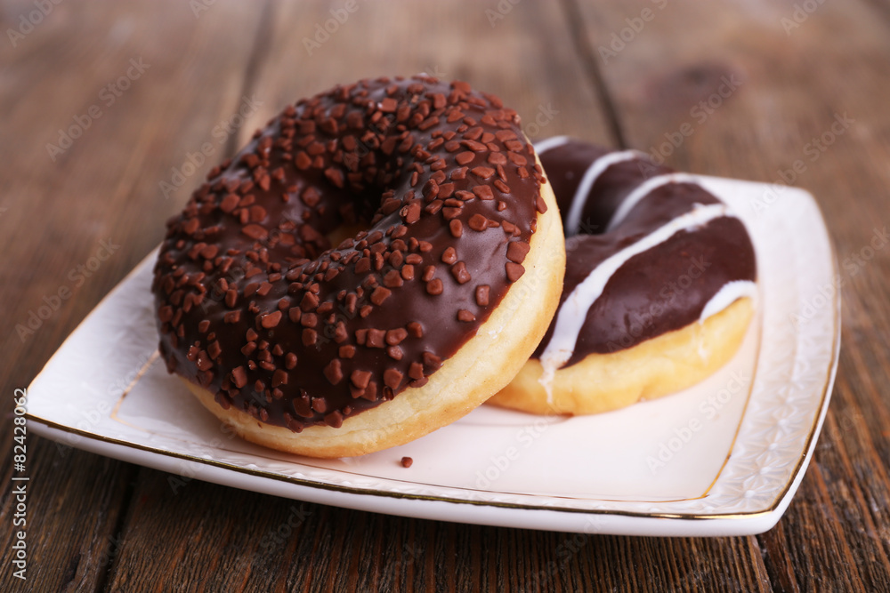 Delicious donuts with icing on plate on wooden background