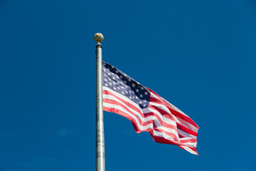 Wall Mural - American Flag Flying from Silver Flagpole on Blue Sky