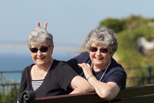 Playful Elderly Twin Sisters On Holiday By The Ocean