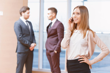 Wall Mural - Blond young business woman standing in front of two men talking 