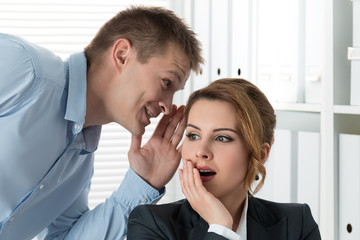 Young man telling gossips to his woman colleague