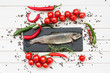 Trout fish on black cutting board with cherry tomatoes