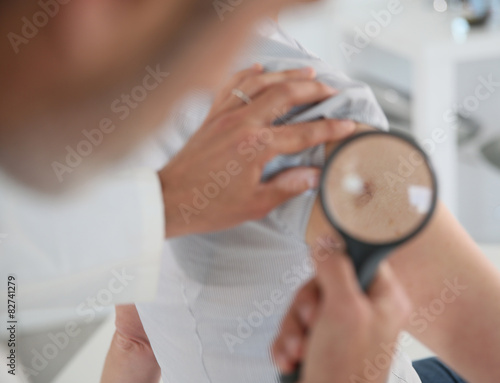 Fotografie, Obraz Dermatologist looking at woman's mole with magnifier