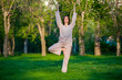 © satyrenko - Practicing yoga in the morning, with trees  background