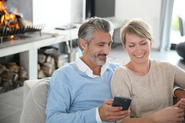 Wall Mural - Mature couple at home having fun using smartphone