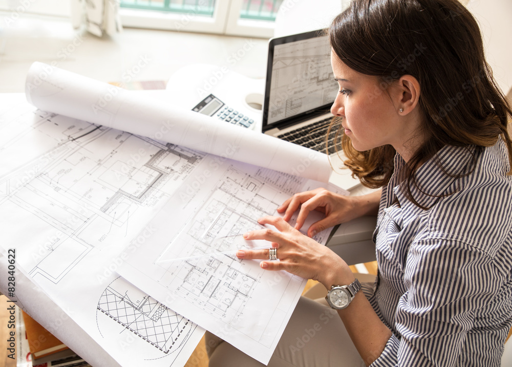 Female architect working at home.She looking at blueprint. - obrazy, fototapety, plakaty 