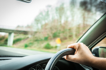 Male driver hands on steering wheel of a car and road