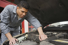 Hispanic Male Auto Mechanic Under Hood Of Car