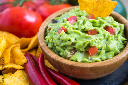 Fotografie, Obraz Guacamole in Wooden Bowl with Tortilla Chips and Ingredients