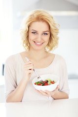 Poster - Young woman eating salad in the kitchen