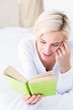 © WavebreakmediaMicro - Smiling blonde woman lying on the bed and reading a book