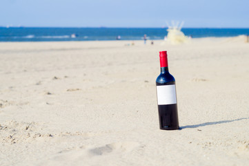 The bottle of red wine with white label on the sunny beach