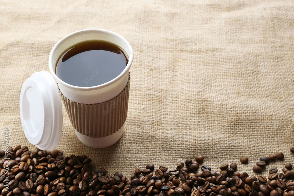 Paper cup of coffee with beans on sackcloth close up