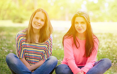 Two young girl friends sitting on grass at summer day