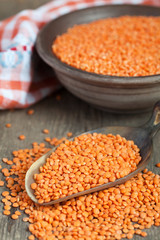 Wall Mural - Dry red lentils in a clay bowl and in a scoop on wooden table