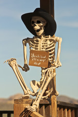 A Cowboy Skeleton Sits Against a Post
