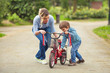 Cute little boy and his mother playing with bicycle in a park