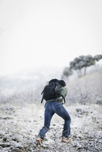 A Man Running Up A Slope In The Mountains Carrying A Rucksack.