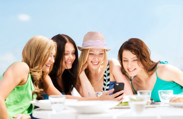 Canvas Print - girls looking at smartphone in cafe on the beach