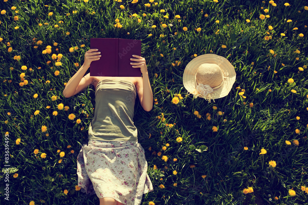 Girl lying in grass, reading a book. - obrazy, fototapety, plakaty 
