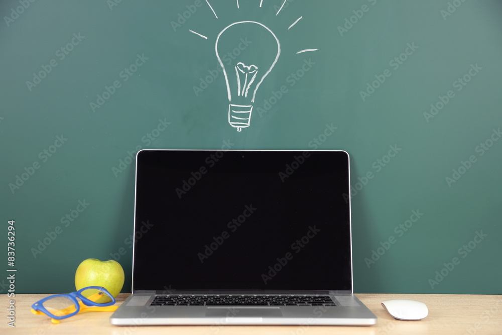 Laptop on table, on green blackboard background