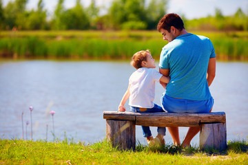 Wall Mural - happy father and son sitting on the river bank