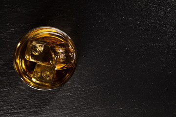 Canvas Print - Glass of whiskey with ice on black stone