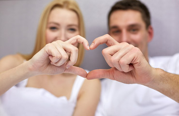 Canvas Print - smiling couple in bed making heart shape gesture