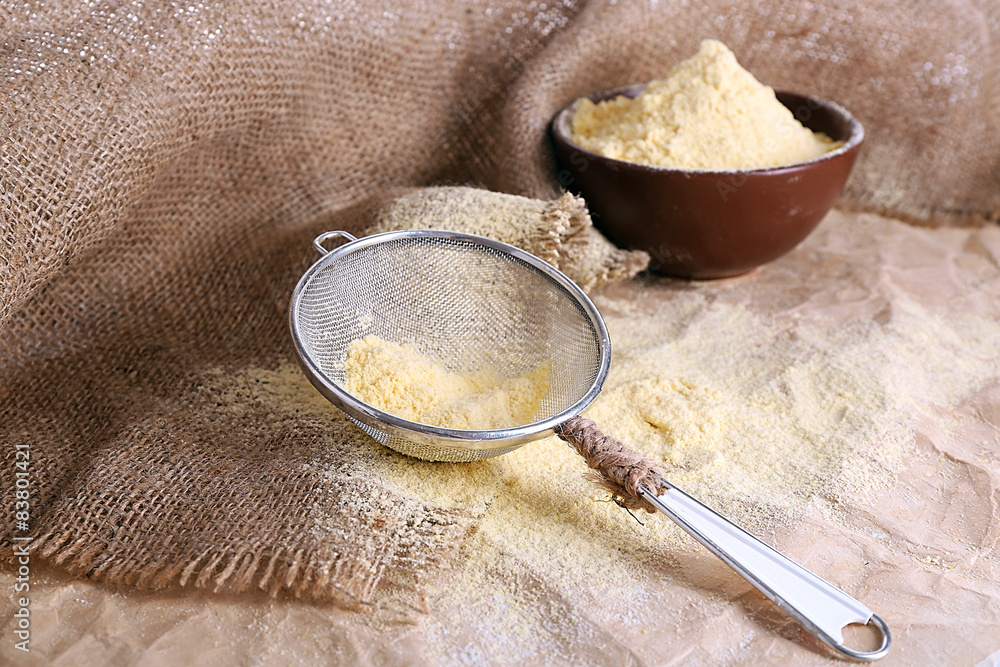 Flour in bowl with sieve on burlap cloth background