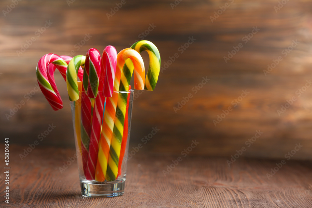 Colorful candy canes in glass on table on wooden background