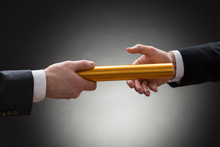 Two Hands Passing A Golden Relay Baton