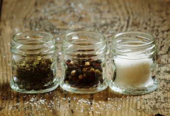 Spices: salt, pepper and herbs in small glass jar on a wooden ta