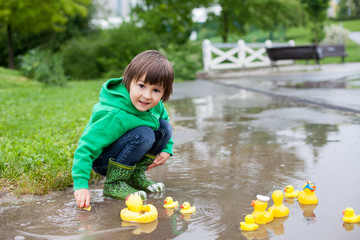 Poster - Little boy, jumping in muddy puddles in the park, rubber ducks i