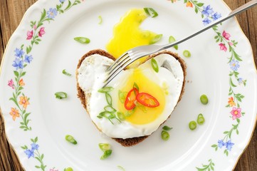 Fried egg heart rye sandwich with scallion, chili and fork on wh