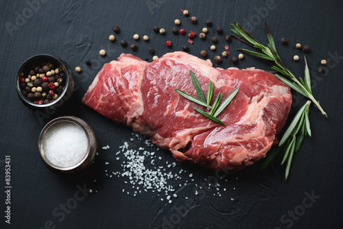 Fényképezés Raw ribeye steak with seasonings over black wooden surface