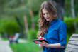 © satyrenko - Side view of a young woman using  tablet computer on  park bench