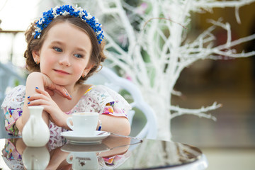 portrait of little girl in a floral dress drinking tea
