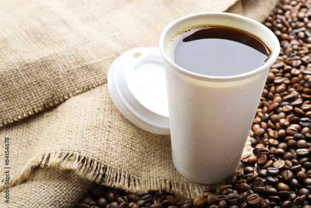 Paper cup of coffee with beans on sackcloth close up