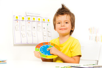 Smiling boy holding colorful carton clock sitting