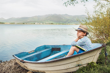 Wall Mural - Dreaming boy in old boat at the lake coast