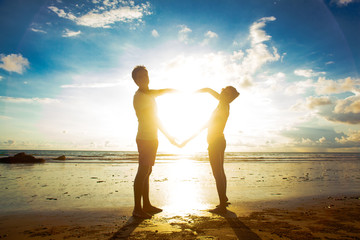 Wall Mural - sunset silhouette of young couple in love holding hands at beach