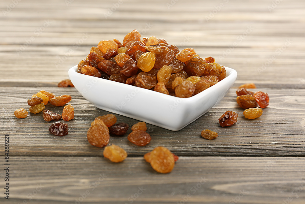 Raisins in saucer on wooden table, closeup