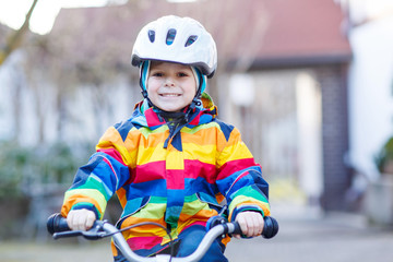 Poster - kid boy in safety helmet and colorful raincoat riding bike, outd