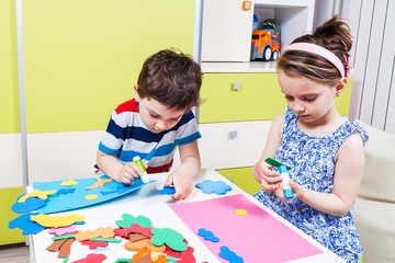 Two preschool child create a picture with foam shapes