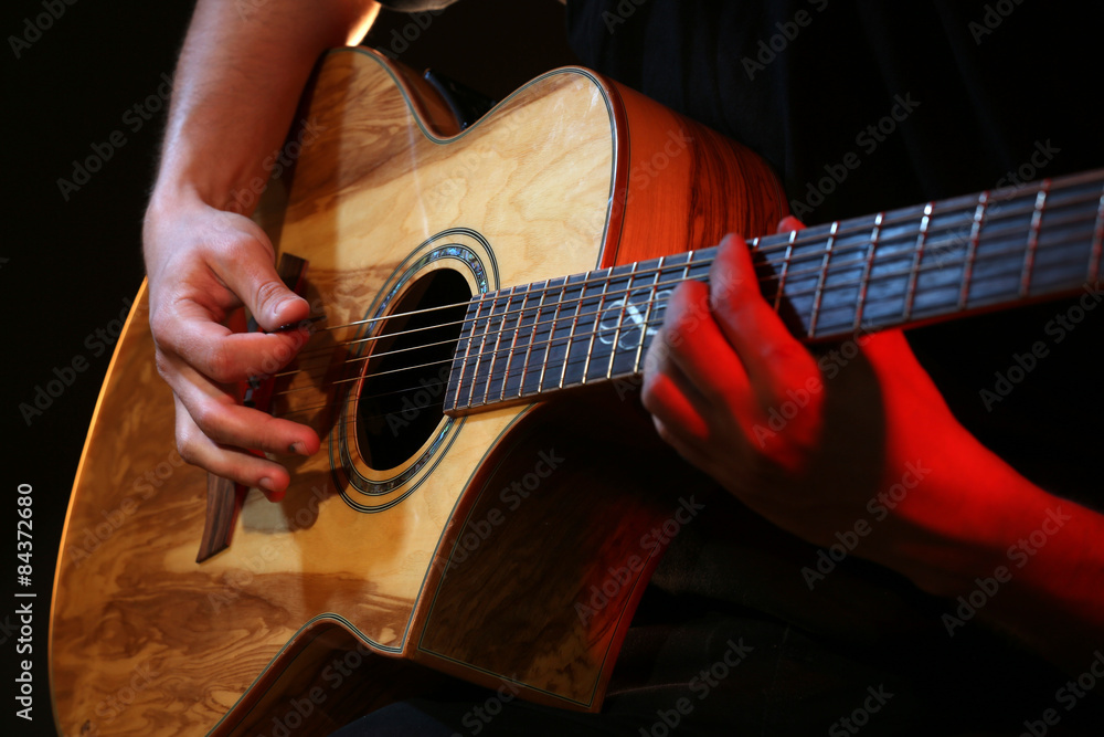 Young man playing on acoustic guitar close up